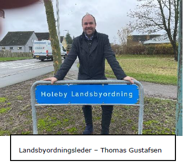 Landsbyordnings Leder Thomas Gustafsen står og læner sig ind over et skilt hvor der står Holeby Landsbyordning