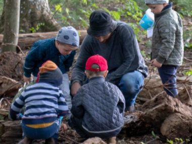 fem Børn og en pædagog undersøger et gammelt træ i skovbørnehaven.